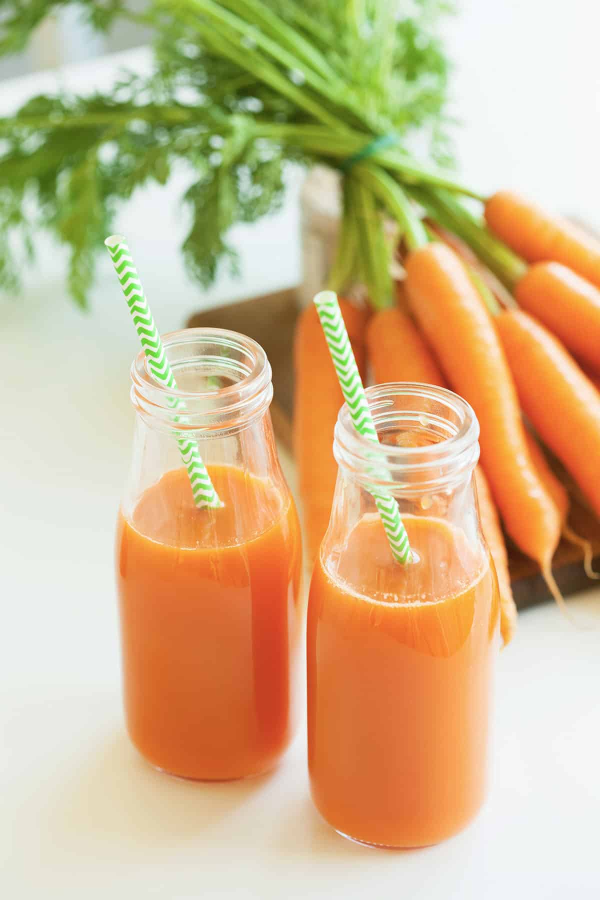 fresh carrot juice and fresh carrots in the background with green striped straws